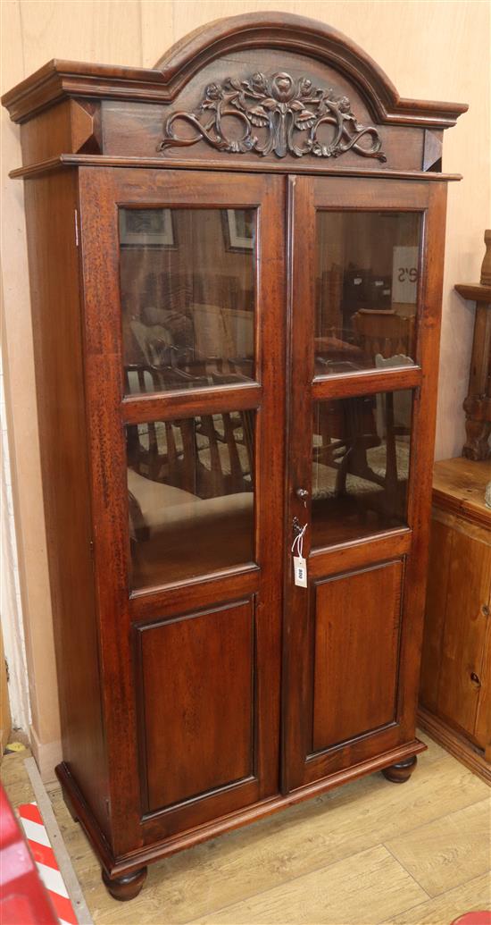 A carved hardwood cabinet with domed topped enclosed by glazed doors, W.96cm